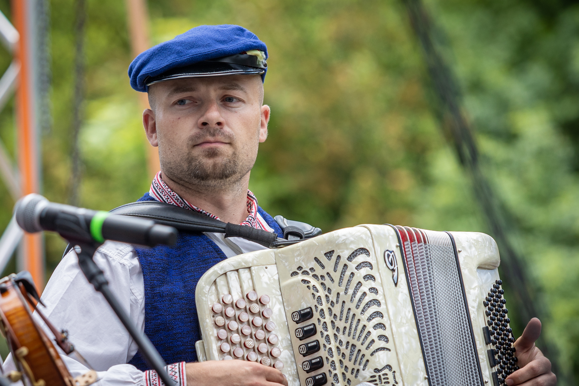 Zdjęcie. Mężczyzna z kulkudniowym zarostem w czapce z daszkiem gra na akordeonie.