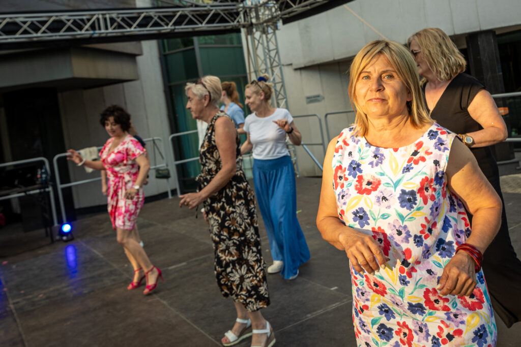 Zdjęcie. Grupa kobiet stoi w dwóch rzędach na scenie letniej KCK. Wszystkie tańczą.