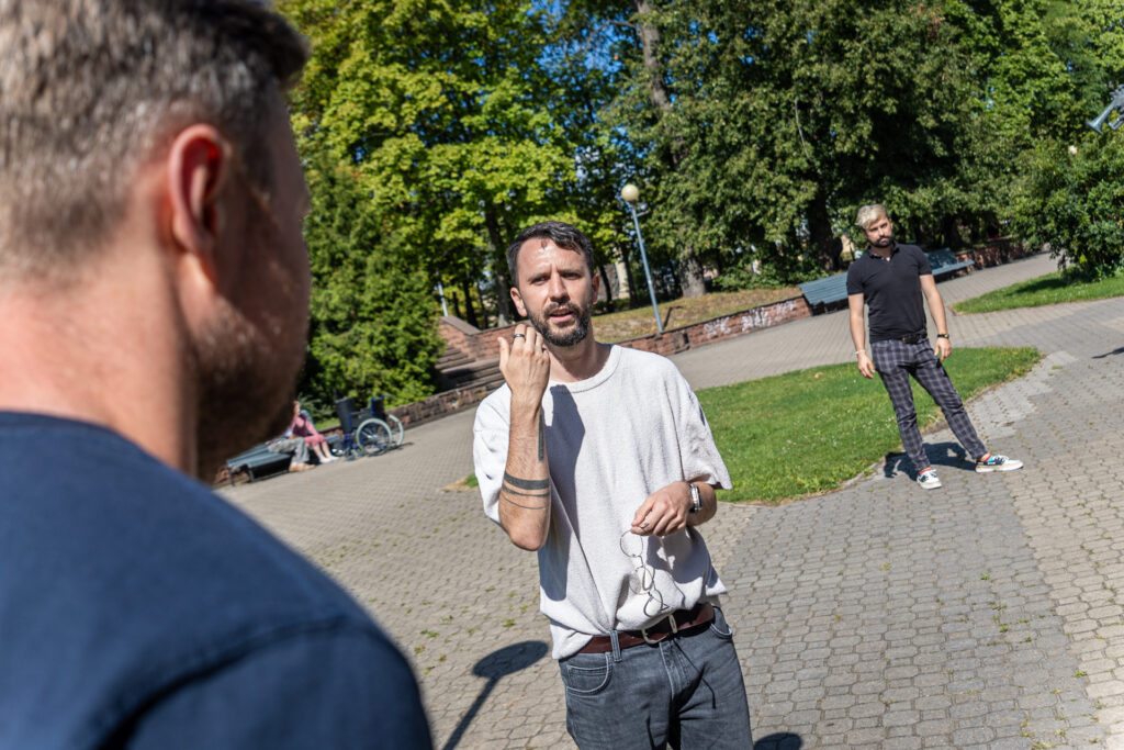 Zdjęcie. Mężczyzna z brodą tłumaczy coś drugiemu mężczyźnie.