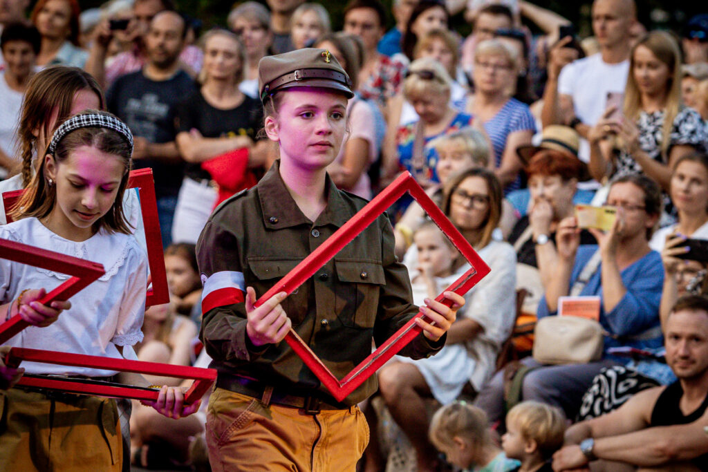 Zdjęcie. Dziewczyna w mundurze i czapce harcerskiej trzyma czerwoną pustą ramkę do zdjęć.