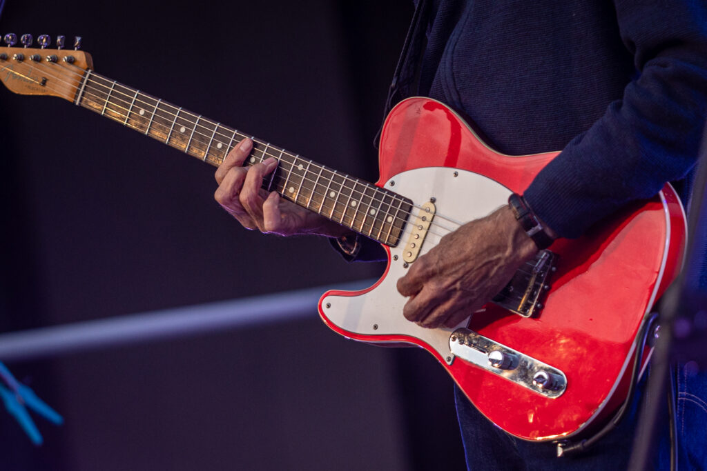 Zdjęcie. Czerwona gitara elektryczna i dłonie grającego na niej mężczyzny.