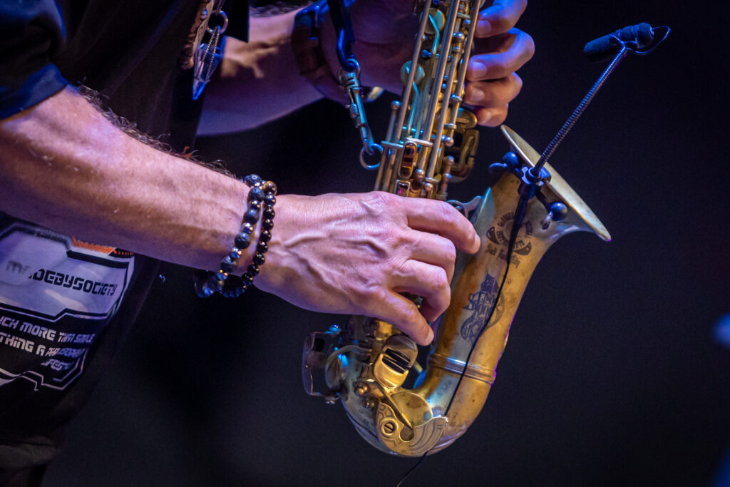 Zdjęcie. Tuba saksofonu i dłonie grające na instrumencie.
