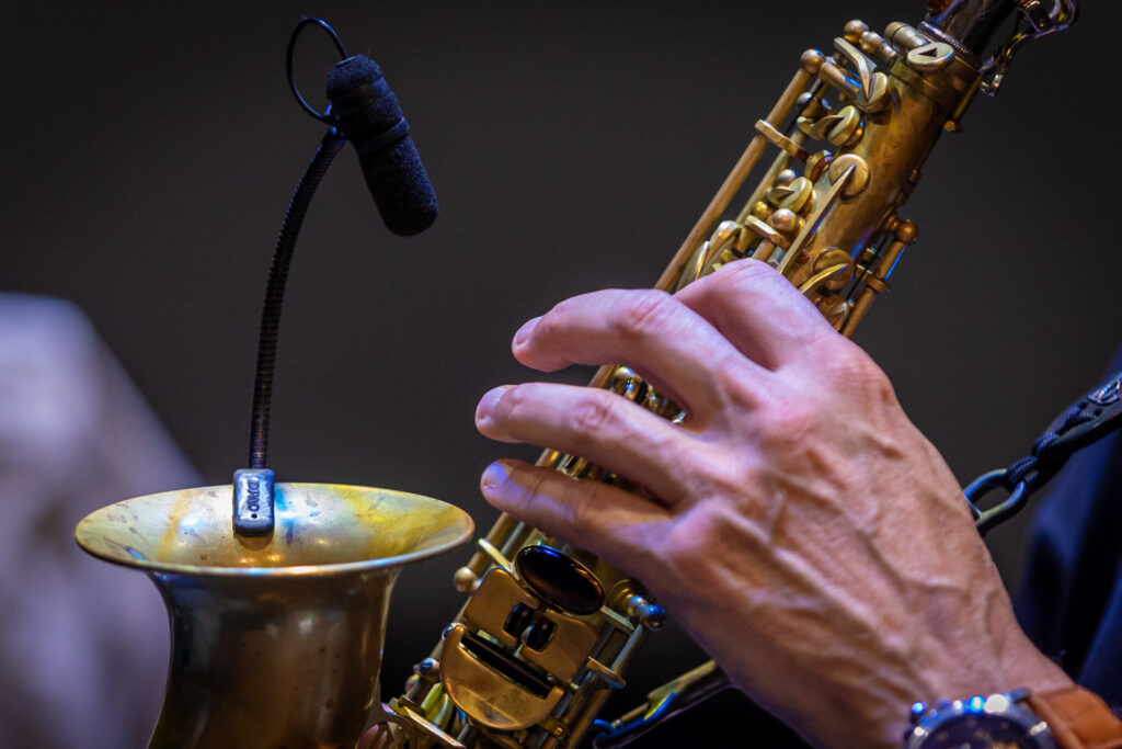 Zdjęcie. Dłoń naciskająca klapki na metalowym instrumencie dętym.