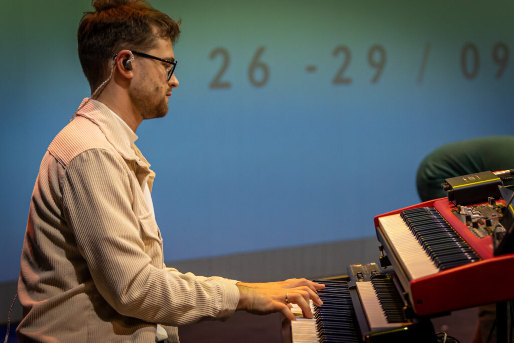 Zdjęcie. Mężczyzna w jasnej koszuli gra na instrumencie klawiszowym.