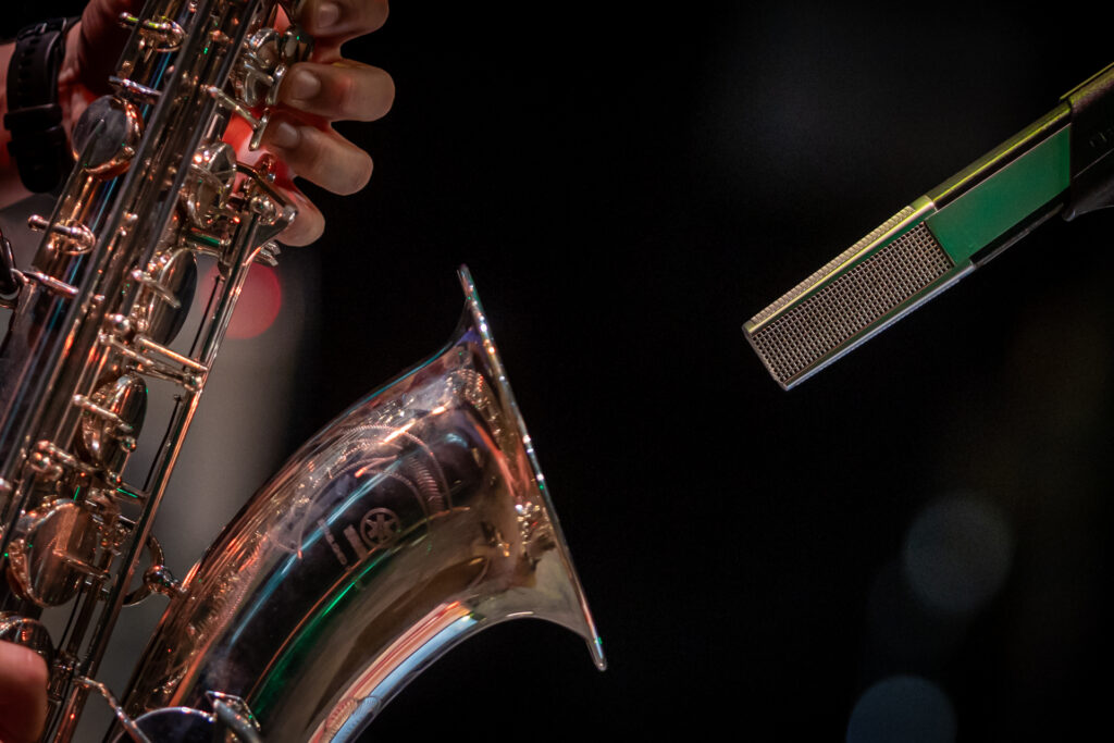Zdjęcie. Tuba saksofonu. Przed nią skierowany na instrument prostokątny mikrofon.