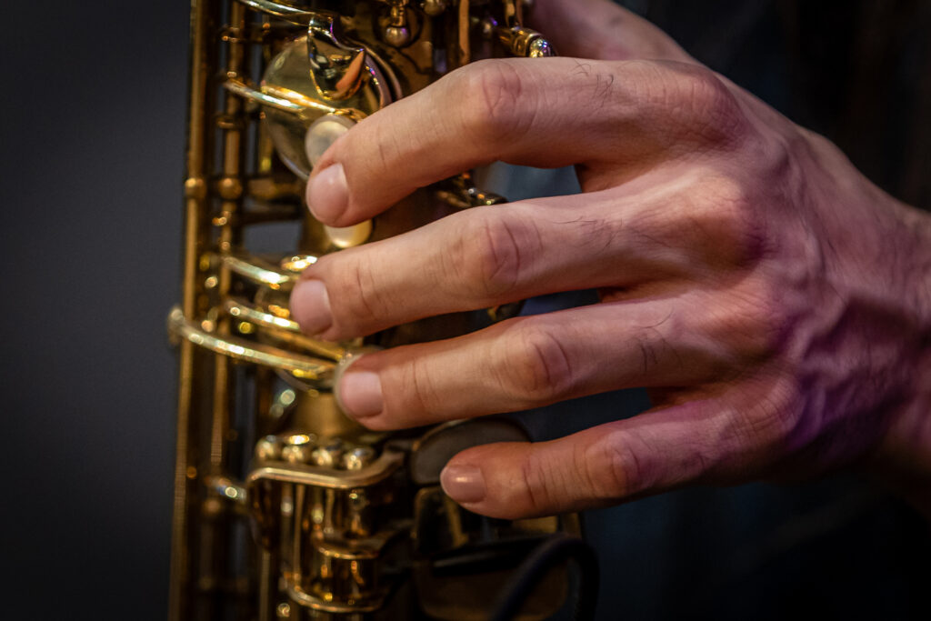 Zdjęcie. Dłoń męska naciskająca okrągłe przyciski złotego instrumentu dętego.