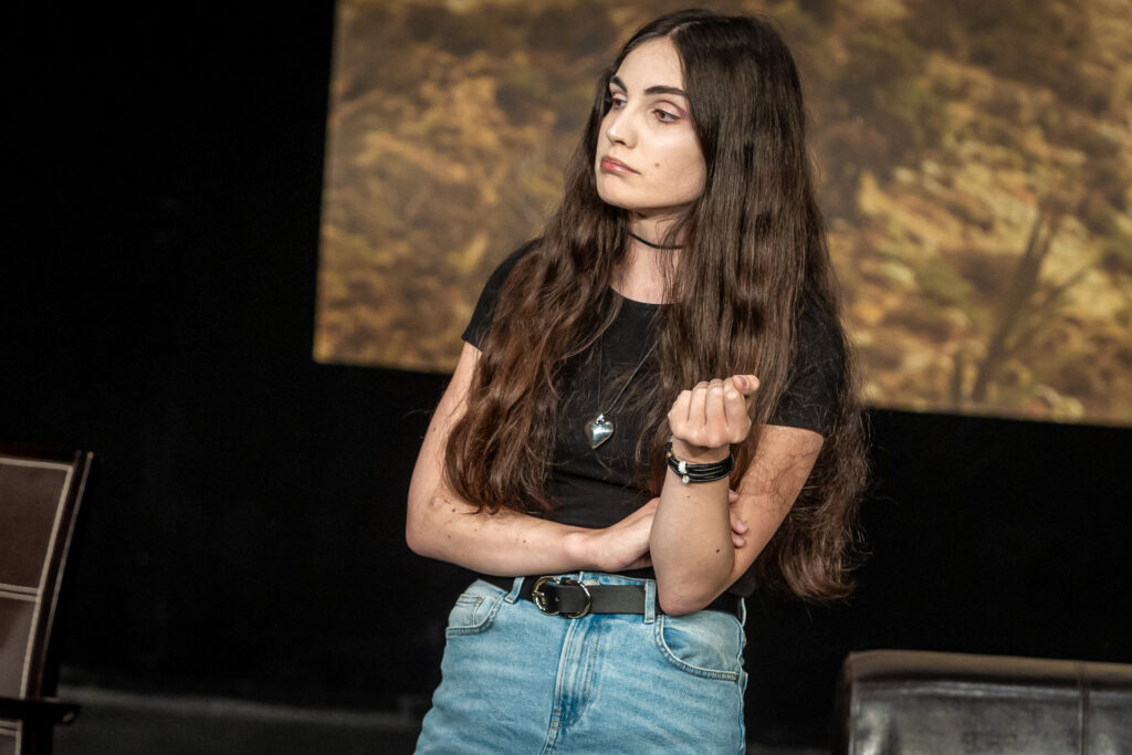Zdjęcie. Brunetka w czarnej podkoszulce i dżinsach patrzy przed siebie. Lewą rękę opiera o zgięcie łokcia prawej.