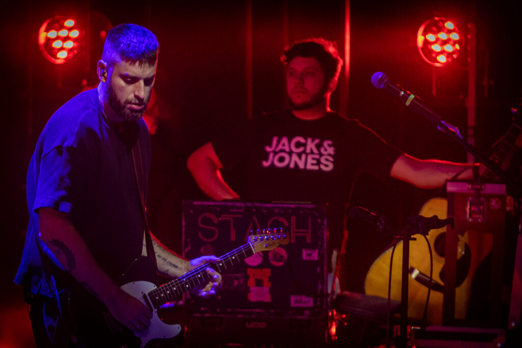 Zdjęcie. Dwójka muzyków na scenie. Jeden z mężczyzn gra na gitarze, drugi na perkusji.