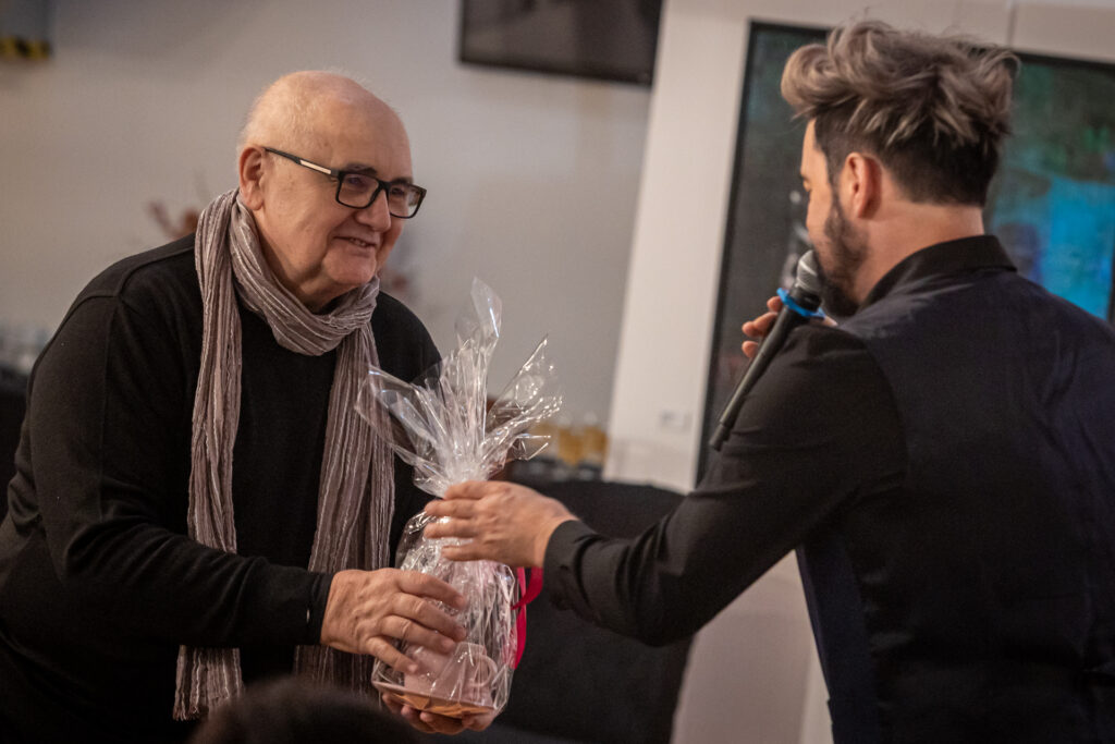 Zdjęcie. Wicedyrektor KCK Artur Wijata wręcza filiżankę siwemu i łysawemu mężczyźnie w okularach.