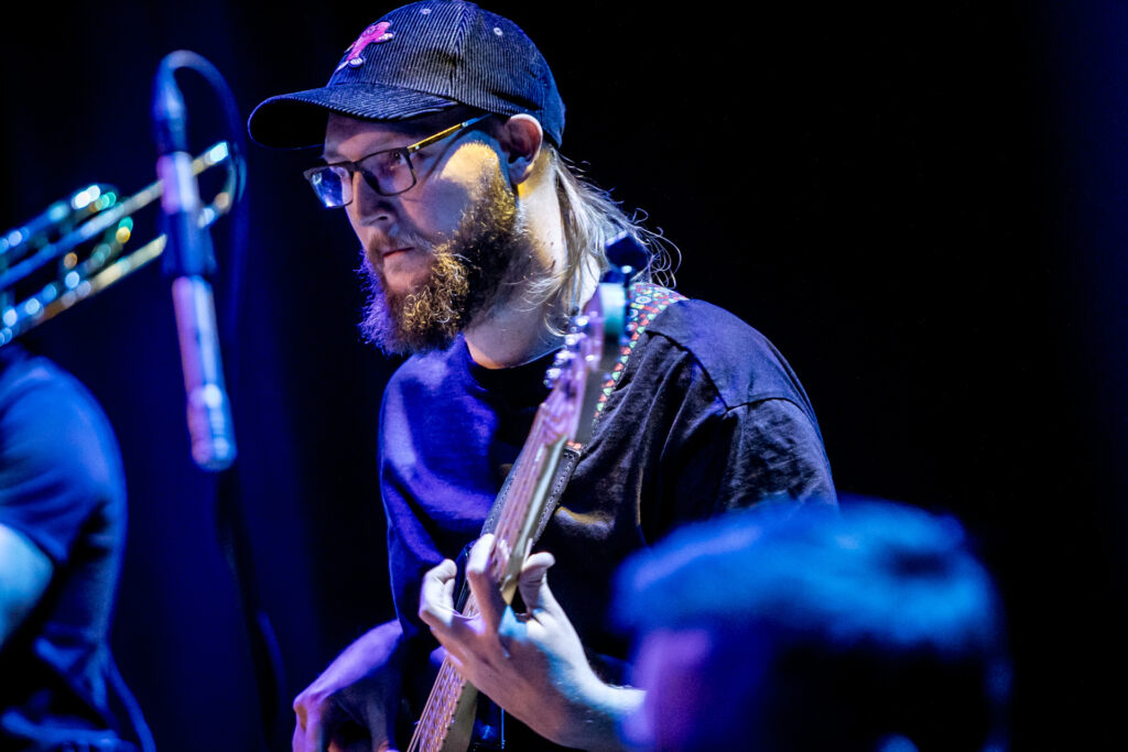 Zdjęcie. Mężczyzna gra na gitarze. Na głowie ma czapkę besjbolówkę.