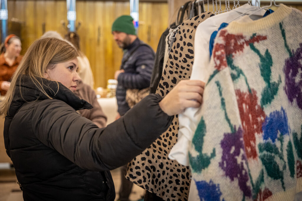Zdjęcie. Blondynka ogląda wzorzysty sweter w duże kwiaty wiszący na wieszaku.
