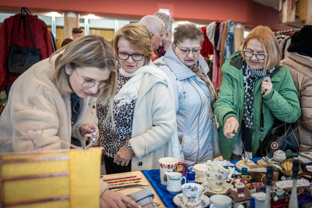 Zdjęcie. Grupakobiet pochyla se nad stlem wypełnionym porcelanowymi drobiazgami i biżuterią.