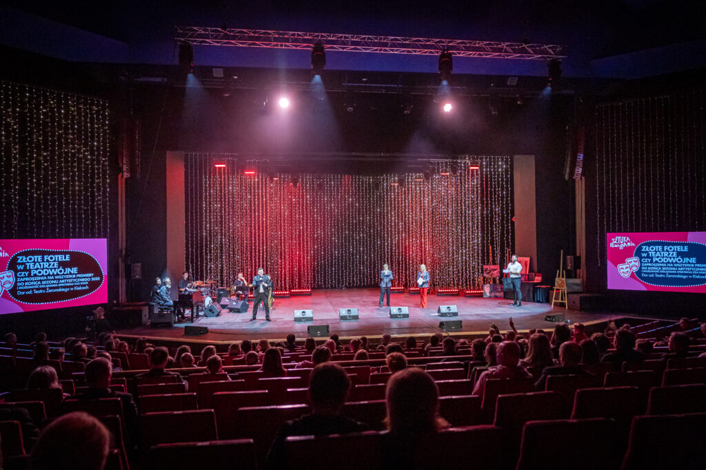 Zdjęcie. Duża SCena KCK. Na scenie ludzie. Z boku dwa ekrany z napisami: Złote fotele w teatrze.