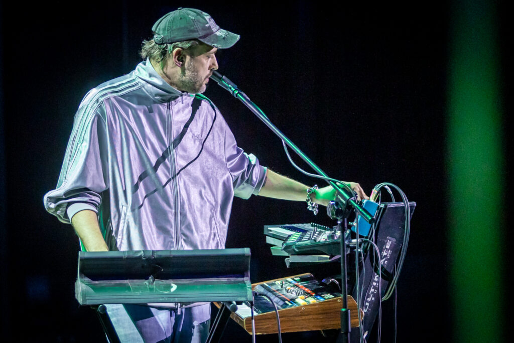 Zdjęcie. Mężczyzna stoi przy instrumentach elektronicznych. Na głowie ma czapkę bejsbolówkę to Tomasz Makowiecki.