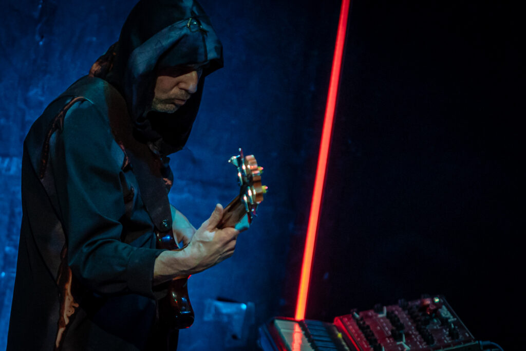 Zdjęcie. Mężczyzna w kapturze na głowie gra na gitarze.