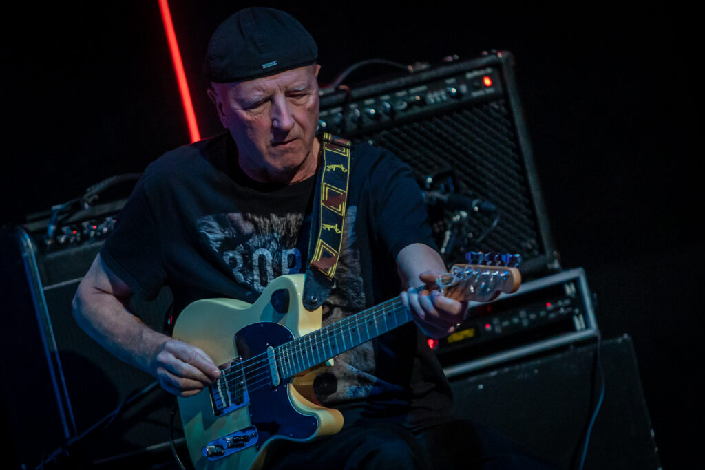 Zdjęcie. Starszy mężczyzna w czapce na głowie gra na gitarze.