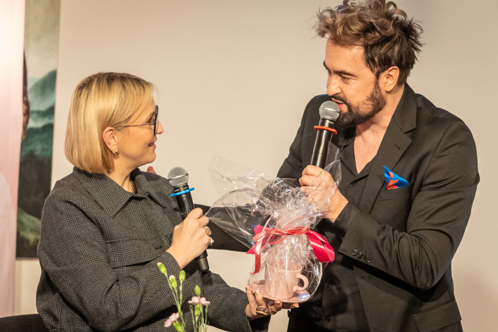Zdjęcie. Wicedyrektor Artur Wijata wręcza różową filiżankę z logo Salonu Kobiet Marcie Kuligowskiej