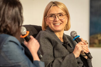 Zdjędynka w okularach patrzy w kierunku brunetki. To Marta Kuligowska podczas Salonu Kobiet. ncie. Uśmiechnięta blo