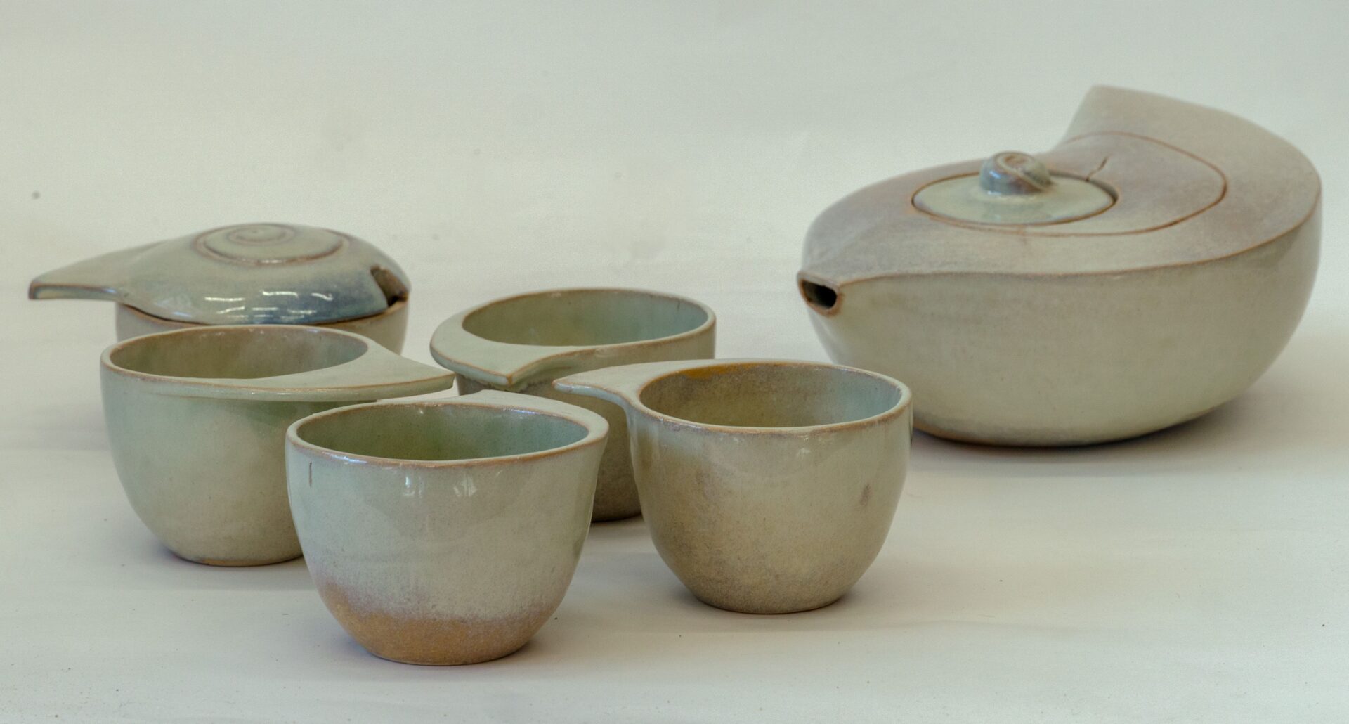 Zdjęcie. Ceramiczny zestaw. Cztery niewielkie miseczki i dwa pojemniki w kształcie muszli. Większy to dzbanek, mniejszy: cukiernica. Zdjęcie zrobione z boku.