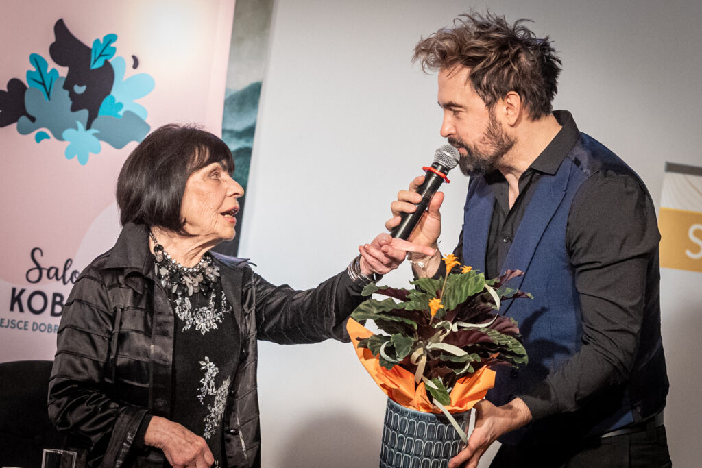 Zdjęcie. Mężczyzna wręcza kobiecie kwiat w doniczce. To wicedyrektor Artur Wijata i Sława Przybylska.