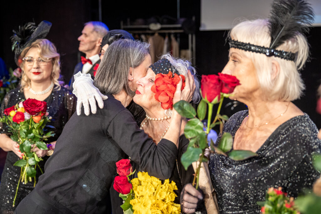 Zdjęcie. Kobieta o prostych siwiejących włosach. To Jolanta Kęćko. Składa gratulacje aktorom teatru bez Sulfera.