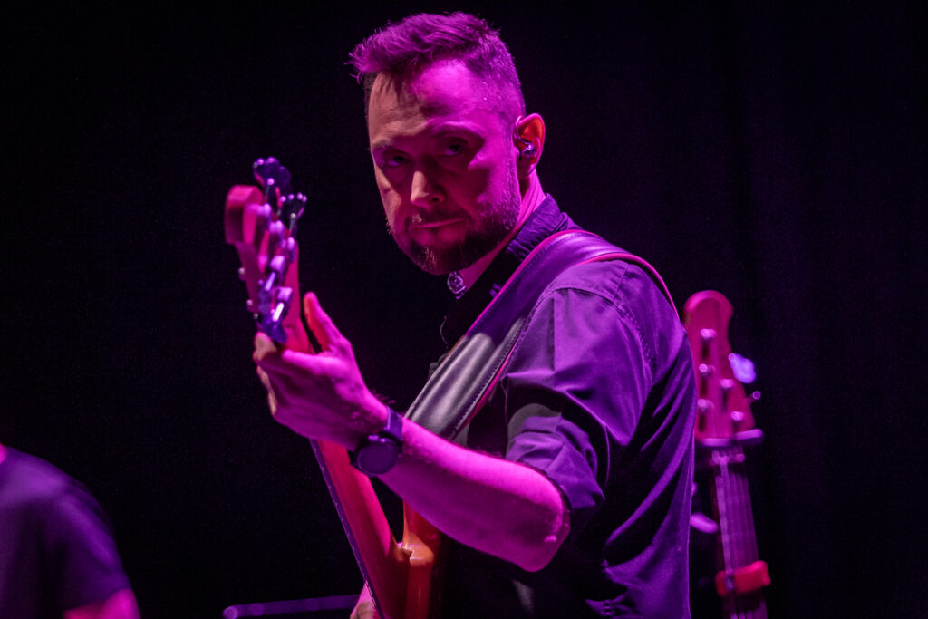 Zdjęcie. Mężczyzna gra na gitarze. Jest oświetlony różowym światłem reflektorów.