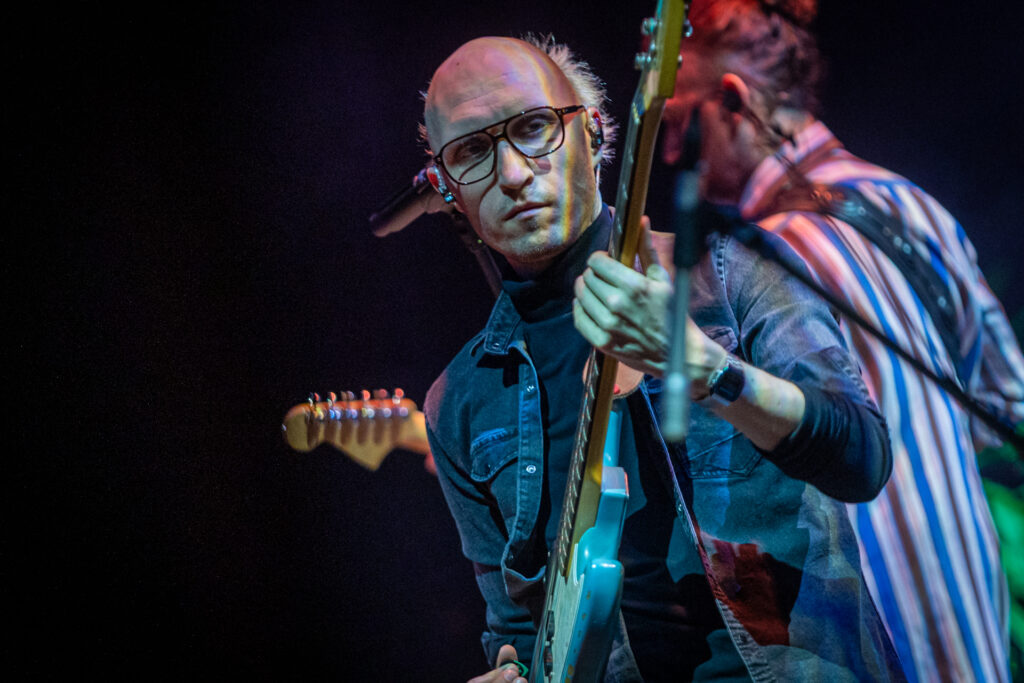 Zdjęcie. Łysawy siwy mężczyzna w okularach gra na gitarze.