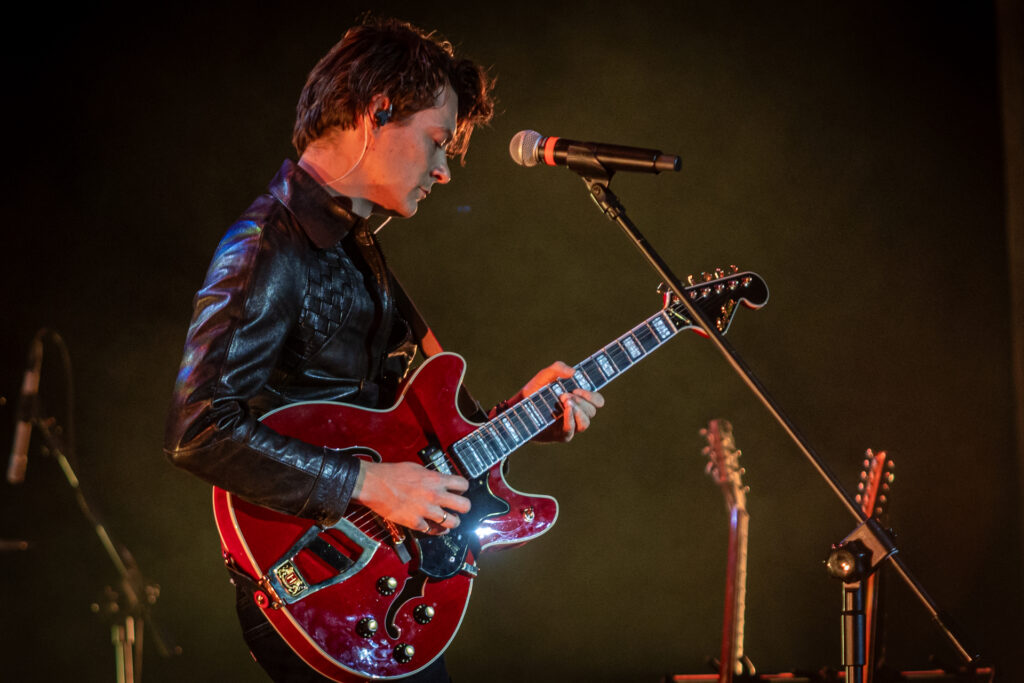 Zdjęcie. Mężczyzna w skórzanej kurtce gra na gitarze. To Tomasz Ziętek.