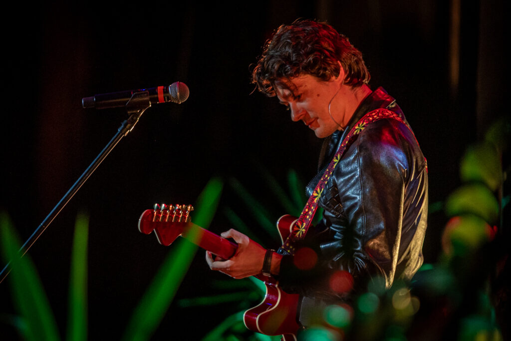 Zdjęcie. Uśmiechnięty mężczyzna gra na gitarze. To Tomasz Ziętek.