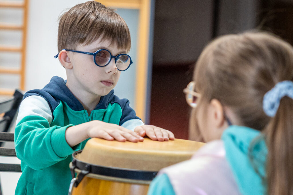 Zdjęcie. Chłopiec w okularach trzyma obie ręce na membranie bębna.