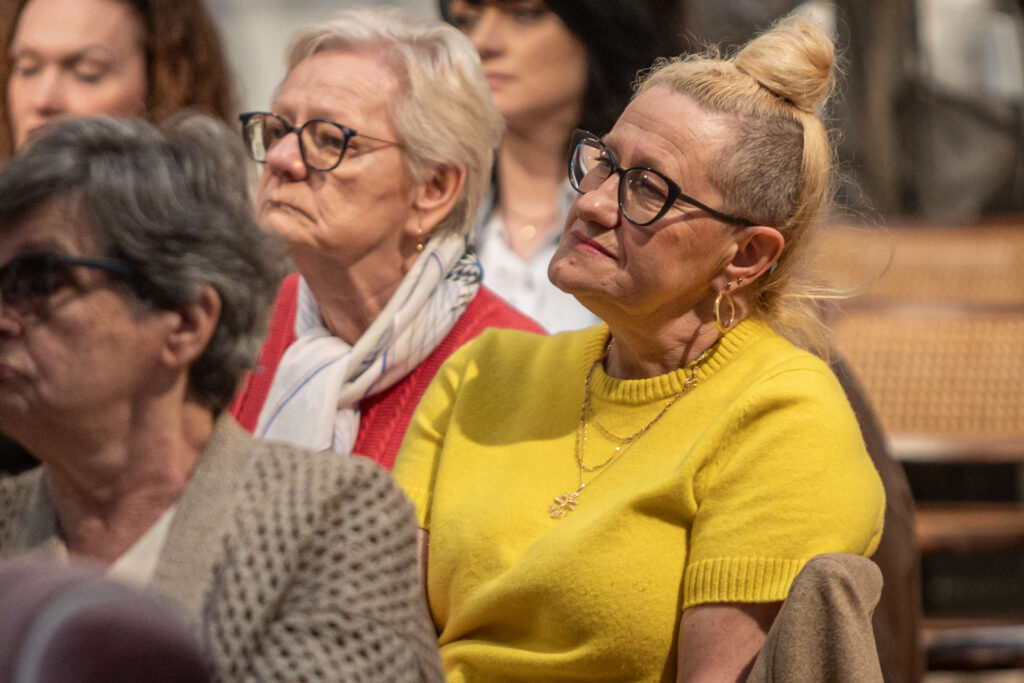 Zdjęcie. Widzka spotkania z Katarzyną Bosacką w Salonie Kobiet. Pani ma wysoko upięty kok, okulary w ciemnych oprawkach. Jest ubrana w żółtą dzianinową bluzkę.